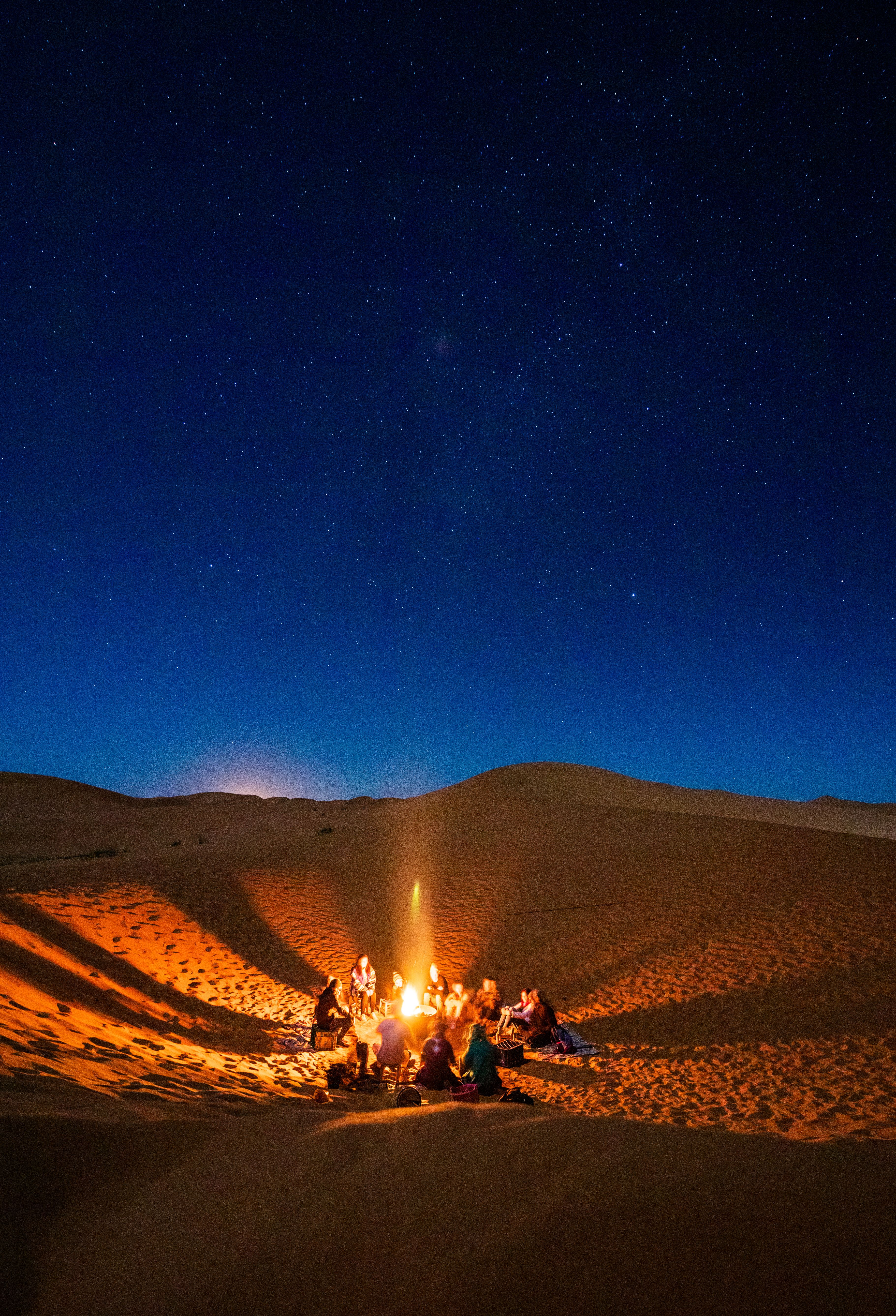 Group of travelers sitting around a campfire in the desert under a starry night sky